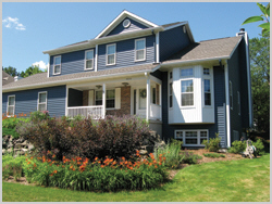 A large home with a well manicured lawn has blue nd white seamless siding.